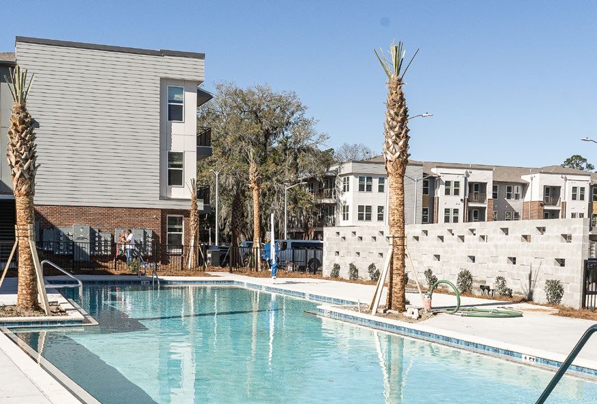 Swimming pool with newly planted palm trees and an exterior image of the apartments. 