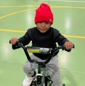A little boy on a bike smiles at the camera.