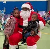 A man dressed up as Santa poses with two children.