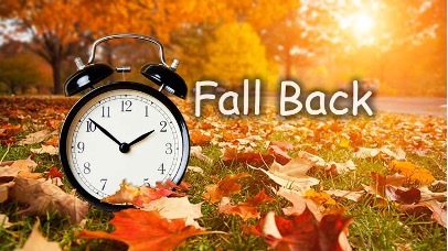 A clock sitting on autumn leaves with text that reads: Fall Back.