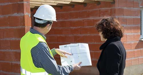 on construction site, man in hard hat with woman in suit looking at blueprints