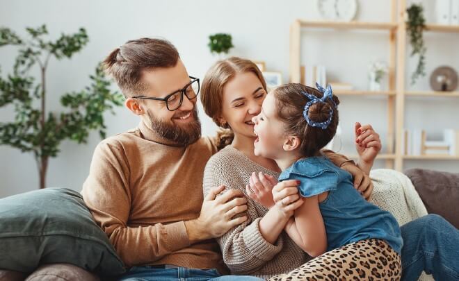 a mom and dad laughing with a young girl while sitting on a couch