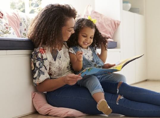 a mom and a young girl reading a book while sitting on the ground