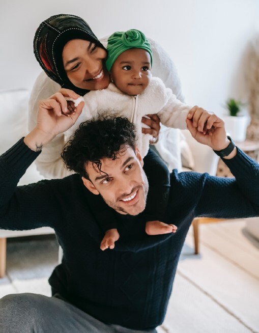 A man holding a baby on his shoulders with a woman standing behind the baby