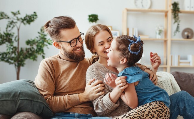 A mom and dad laughing with a young girl while sitting on a couch