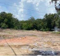 A cleared lot with heavy equipment tracks in the dirt is surrounded by trees