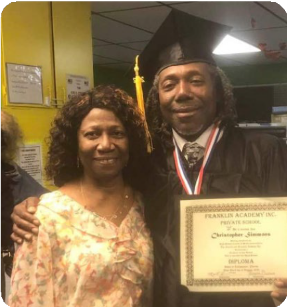 Christopher Simmons, in his graduation cap and gown, has his arm around another person's shoulders and proudly displays his diploma. 