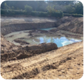 A large empty hole in the ground is slowing filling up with water. 