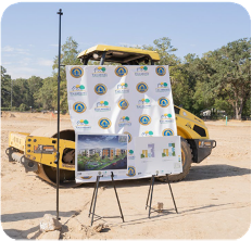 A large display of the Orange Ave. Development sits in front of a road roller.