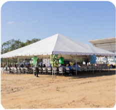 Many people are gathered under a large tent that is outside. 