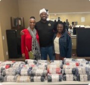 Three people smiling behind stacks of scarves and blankets.