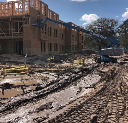 A muddy construction site with a crane being used to attach walls to the exterior of the building.