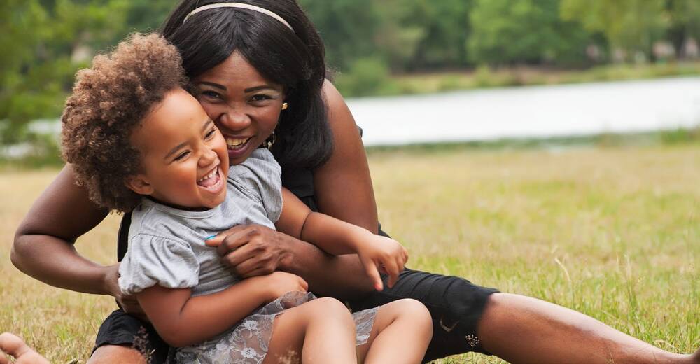 Parent and child laughing in the grass.