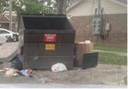 Garbage dumpster with trash set outside of it. 