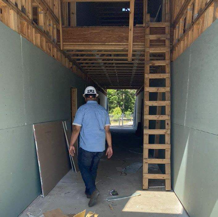 Man in hard hat in hallway with ladder and unfinished walls. 