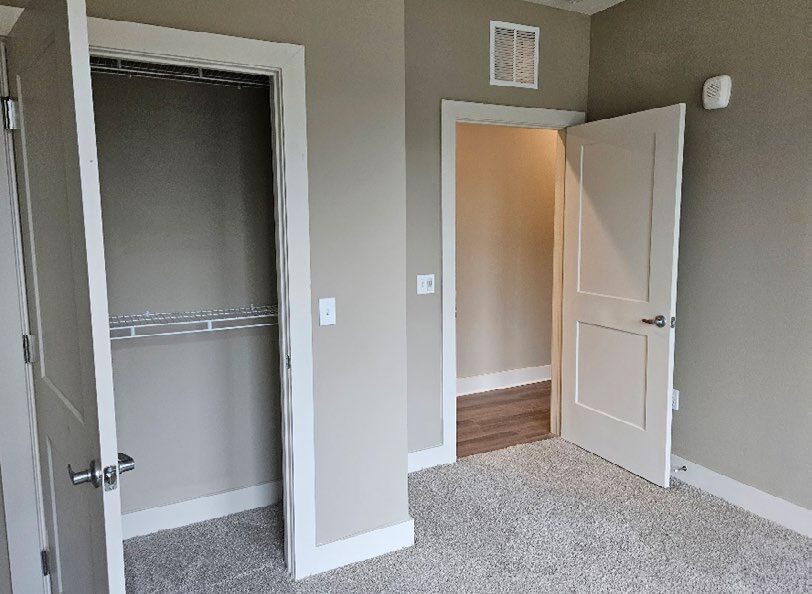 A finished room showing a closet an doorway to a hall.