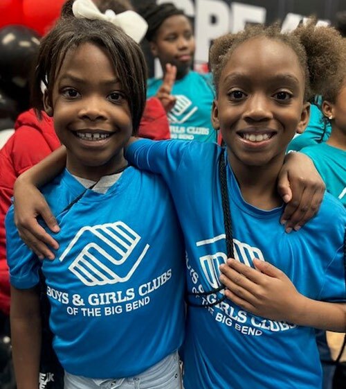 Children with arm around each other's shoulders, smiling at the camera wearing Boys and Girl's Clubs of the Big Bend shirts.