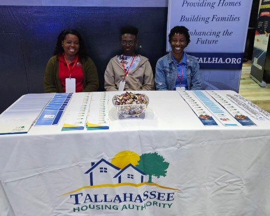 Three women setting at a tradeshow booth representing the Tallahassee Housing Authority.