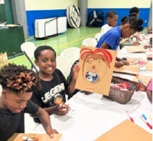 Kids sitting and doing art projects at tables.