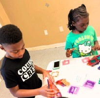 2 kids sit and make art at a table.