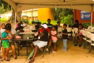 Kids sitting at tables outside under a tent.