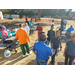 Lots of people have gathered together to get breakfast; a woman is pouring pancake batter onto a flat top grill. 