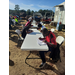 Three plastic tables are set up end to end and there are people sitting at the tables filling out paperwork. 