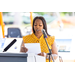 A woman speaks into a microphone while reading off a piece of paper.