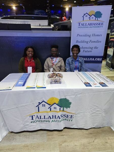 Three people from Tallahassee Housing Authority sitting at a tradeshow table with handouts and literature on the table. 