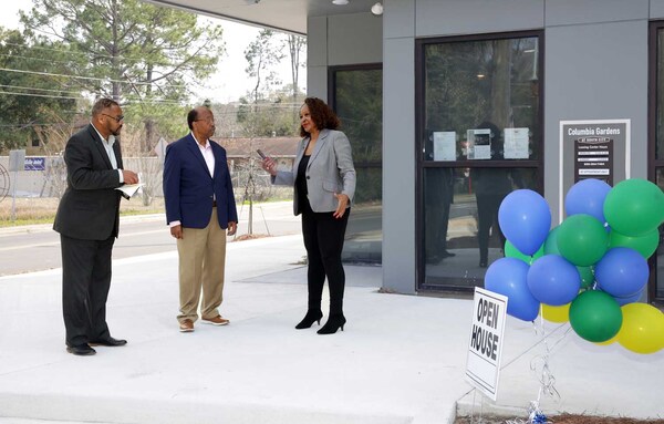Three people talking next to an Open House sign with balloons. 