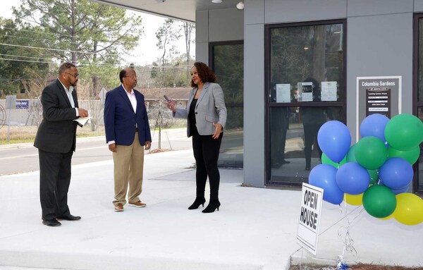 Three people talking next to an Open House sign with baloons. 